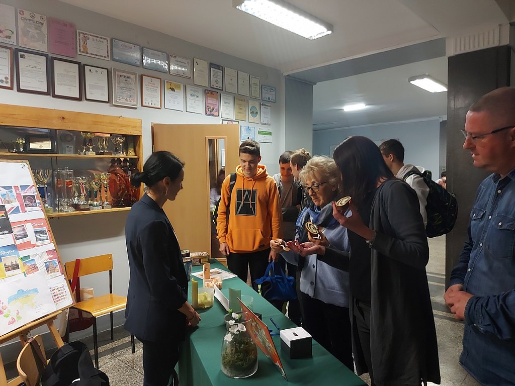 Stoiska z eksponatami. Nauczyciel prezentuje, a uczniowie z zainteresowaniem oglądają. 