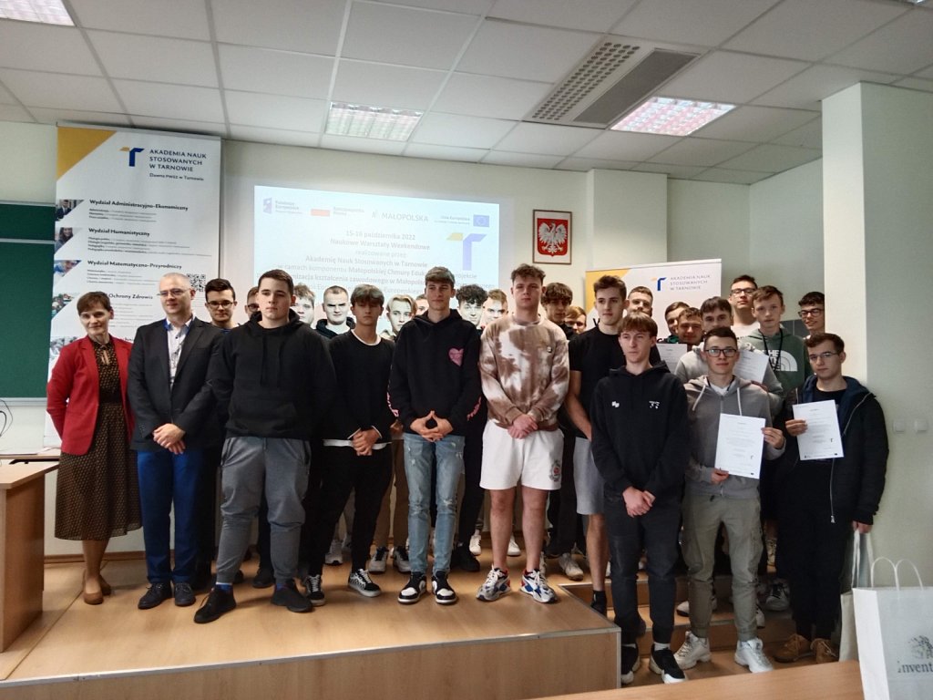 Grupa uczniów w sali konferencyjnej. Za nimi ekran z prezentacją. 