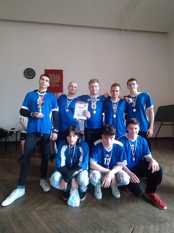 Drużyna ubrana w jednolite niebieskobiałe stroje. Jeden z uczniów trzyma dyplom.